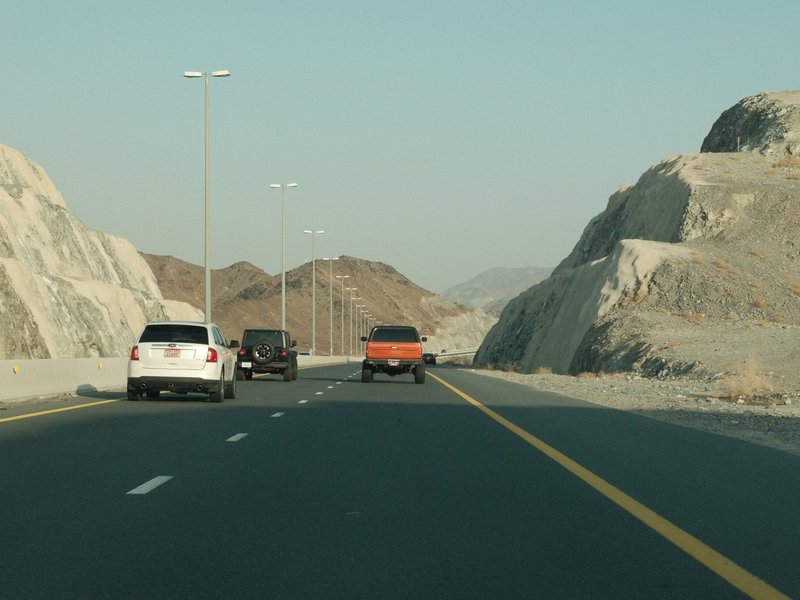 A view of a highway surrounded by rocky hills with vehicles driving on the road.