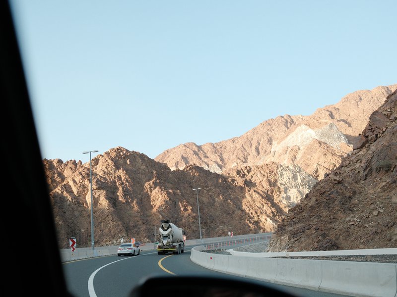 View of a winding road through rocky mountains with a vehicle in the foreground.
