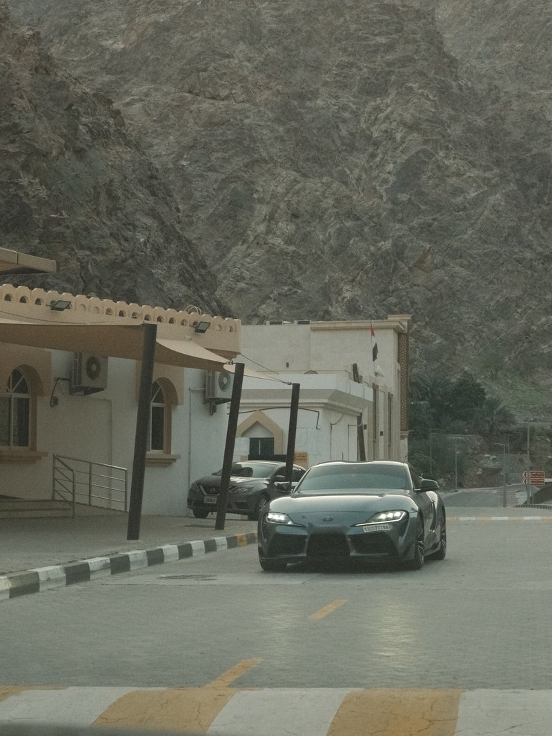 A sleek black sports car driving on a road with rocky mountains in the background.