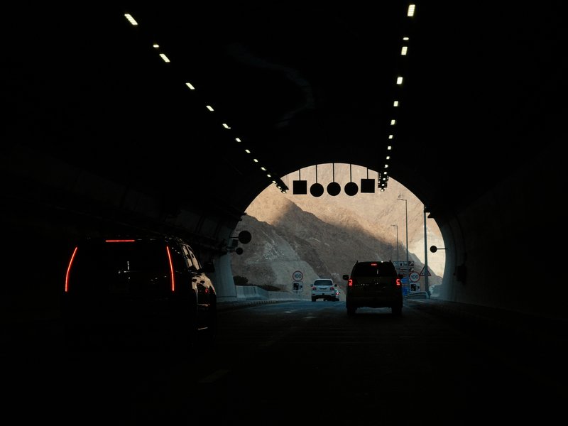 Cars driving through a dark tunnel with light at the tunnel's exit illuminating the scene.