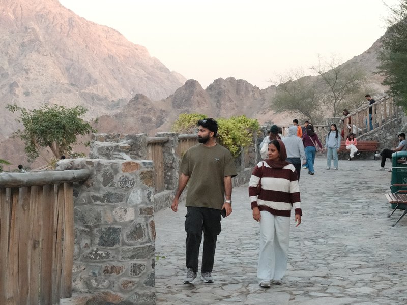 Two people walking on a stone path with mountains in the background during sunset.