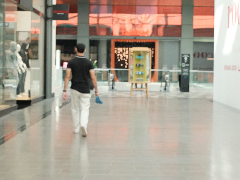 A person walking through a modern shopping mall with bright reflections and storefronts.