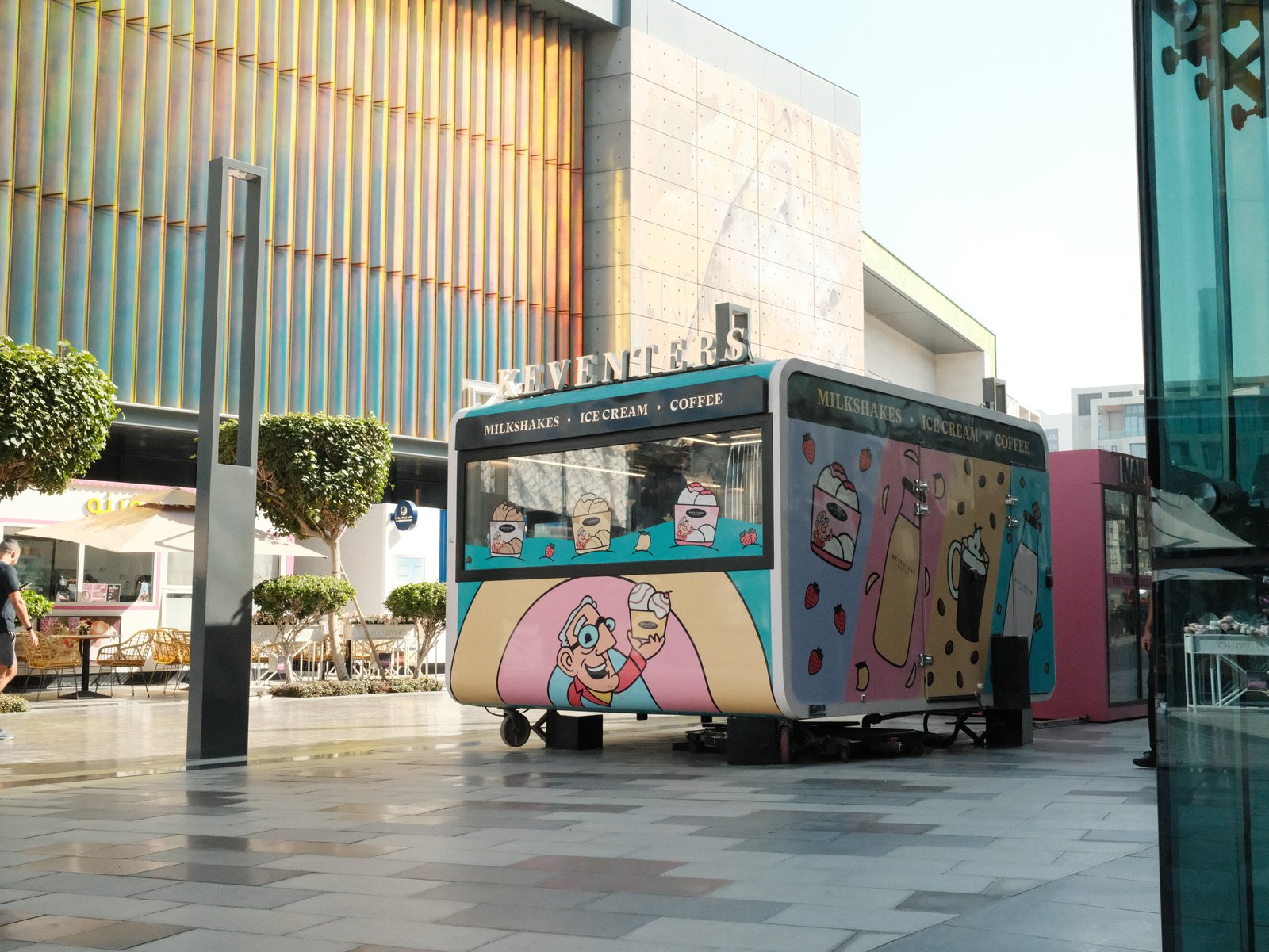 A colourful food truck parked in an urban setting with modern buildings behind, shot on Pastel Portra Chrome