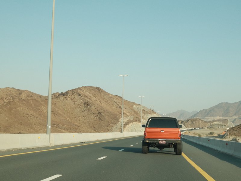 A black pickup truck driving on a highway with brown hills in the background under a clear blue sky.