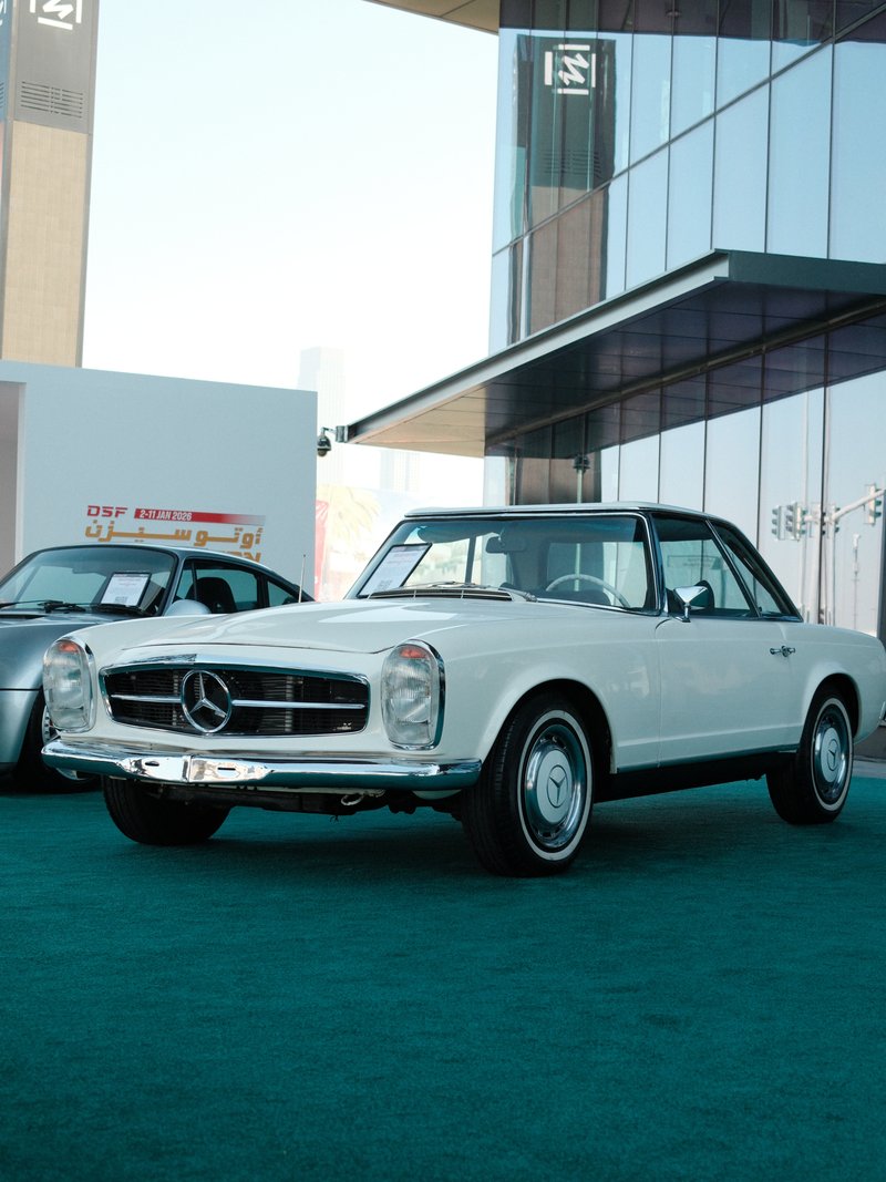 A classic white Mercedes-Benz car parked in front of a modern building with glass architecture.
