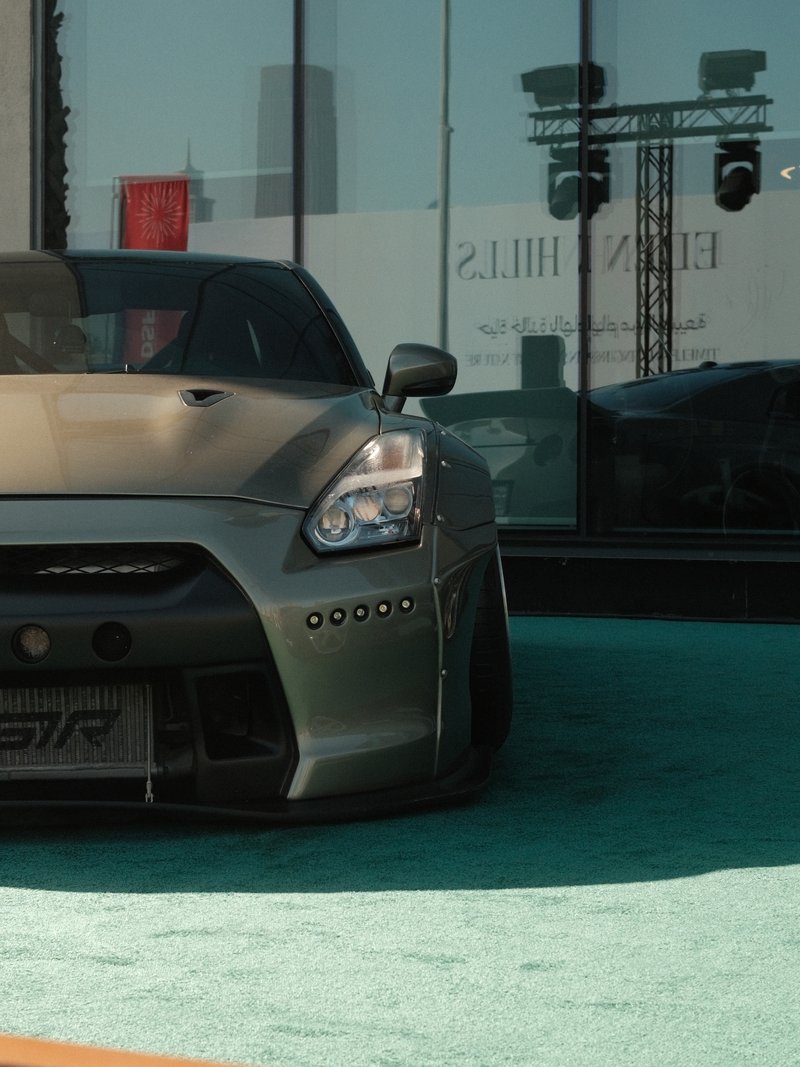 Close-up of a modified sports car parked on a turquoise surface with reflections of buildings.