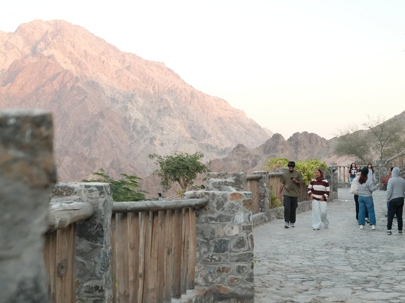 A group of people walking along a stone path with mountains in the background during sunset.