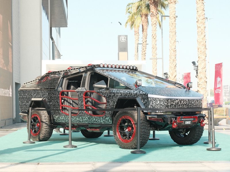 A futuristic armored vehicle displayed outdoors with palm trees in the background.