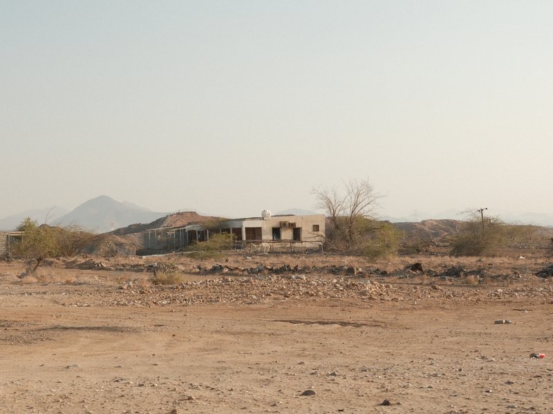 A dilapidated building in a barren landscape with distant mountains under a clear sky.