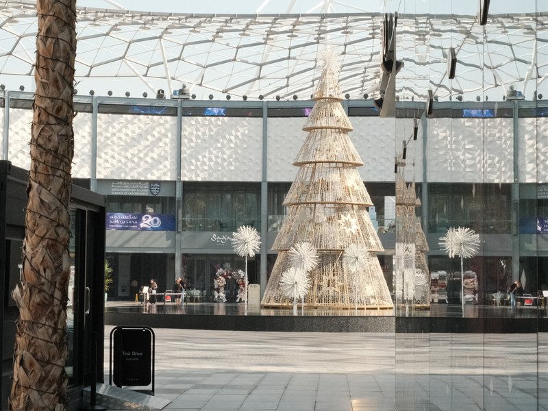 A large decorative Christmas tree in a modern shopping mall with people in the background.