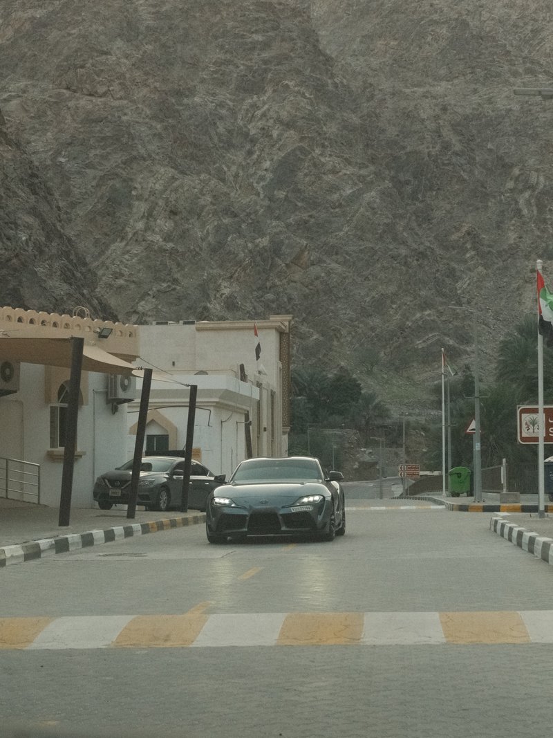 A sleek black car driving on a quiet street with rocky mountains in the background.