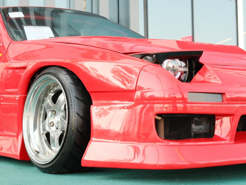 Close-up of a modified red sports car with a sleek body and large wheels, parked indoors.
