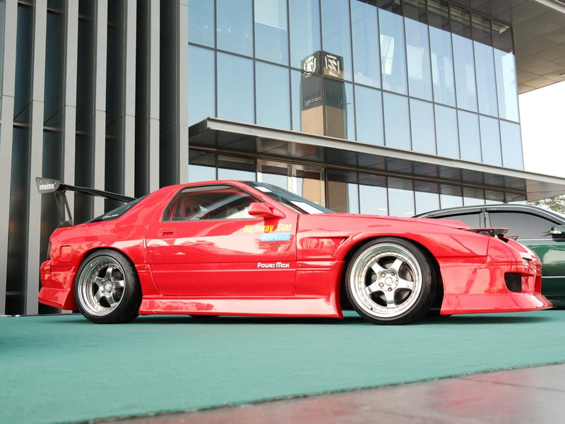 A bright red sports car parked on a green surface in front of a modern building with large windows.
