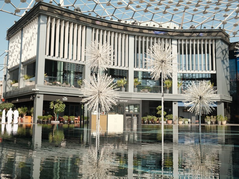 Modern architectural building with reflective water surface and artistic installations in front.