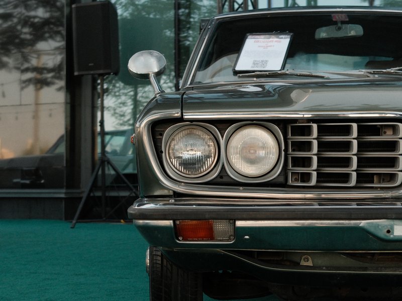 Close-up of a vintage car's front, showcasing headlights and grille against a green backdrop.