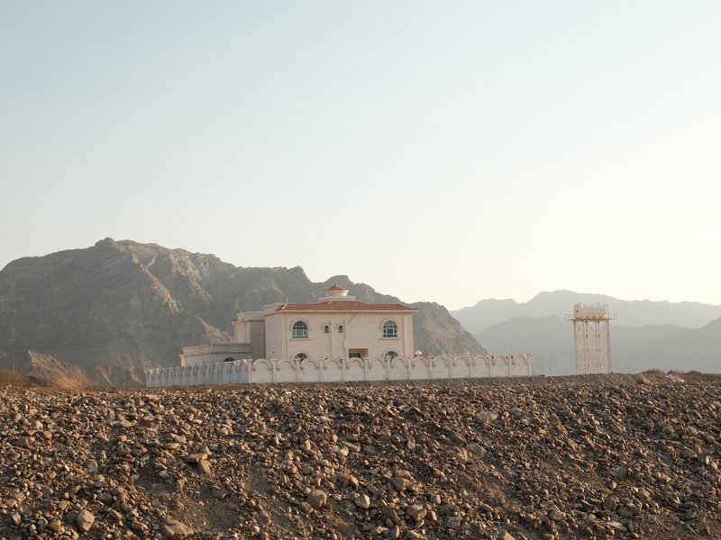 A distant view of a white building against a rocky mountain backdrop under a clear sky.