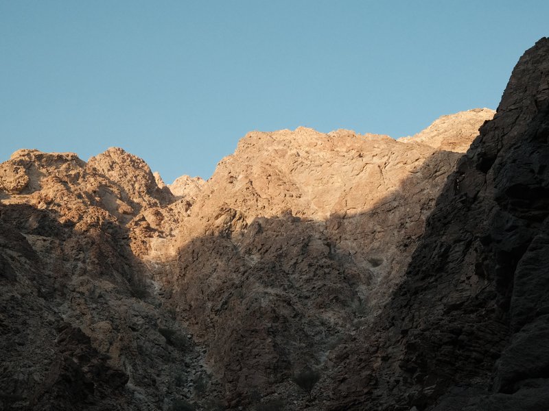 Rocky mountain peaks illuminated by sunlight against a clear blue sky.