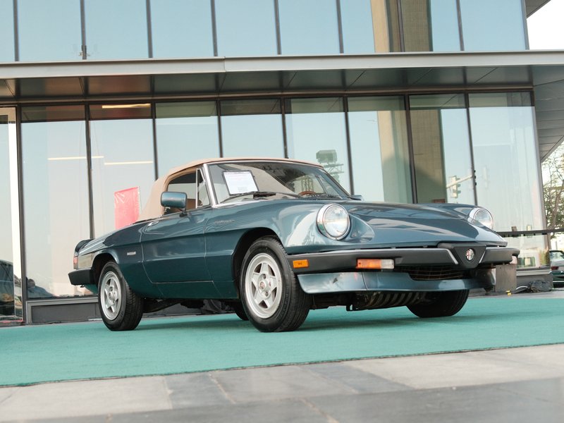 A vintage blue convertible car parked on a green surface in front of a modern glass building.
