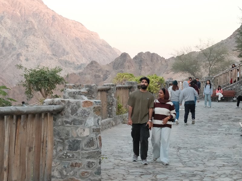 Two people walking along a stone path with mountains in the background during sunset.