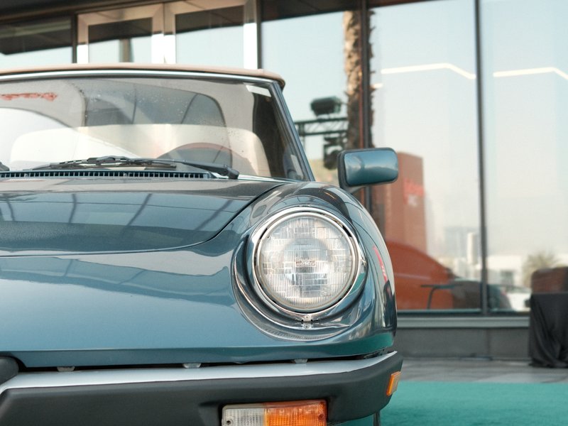 Close-up of a vintage car's front, showcasing its round headlight and sleek design against a modern backdrop.