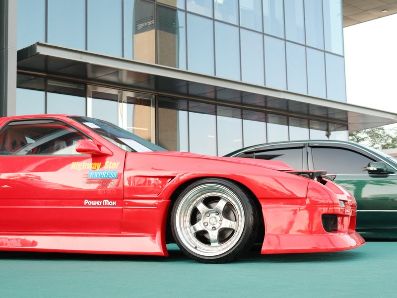 Two modified cars parked in front of a modern glass building, showcasing vibrant colors and sleek designs.