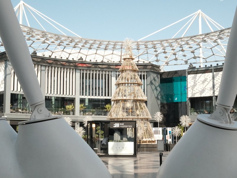 A modern shopping center with a large decorative tree in the center, framed by architectural structures.