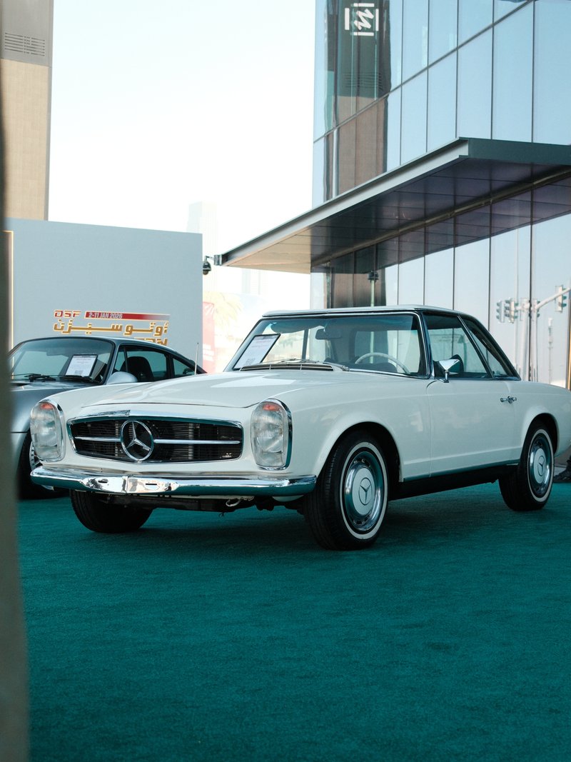 Classic white Mercedes-Benz car parked in front of a modern glass building.
