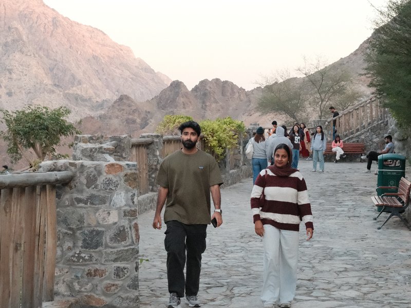 Two people walking along a stone path with mountains in the background during sunset.