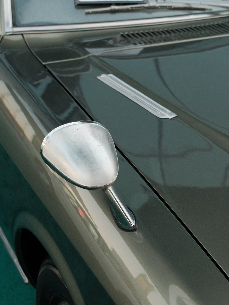 Close-up of a vintage car's side mirror and hood, showcasing its sleek design and reflective surface.