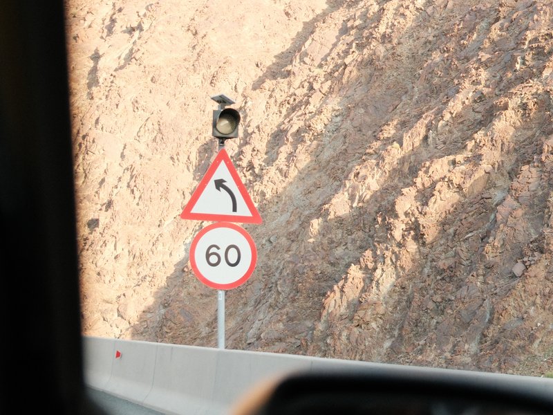 Traffic signs indicating a left curve and speed limit of 60 km/h on a mountainous road.