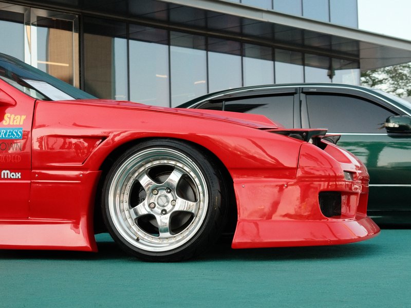 Close-up of a red modified car with a low profile and shiny rims parked beside a green car.