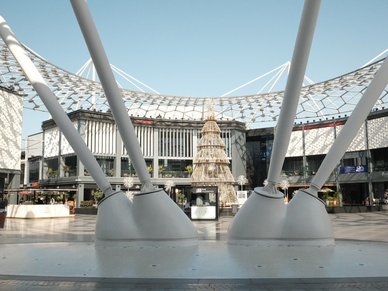 View of a modern plaza with a large Christmas tree and architectural structures in the background.