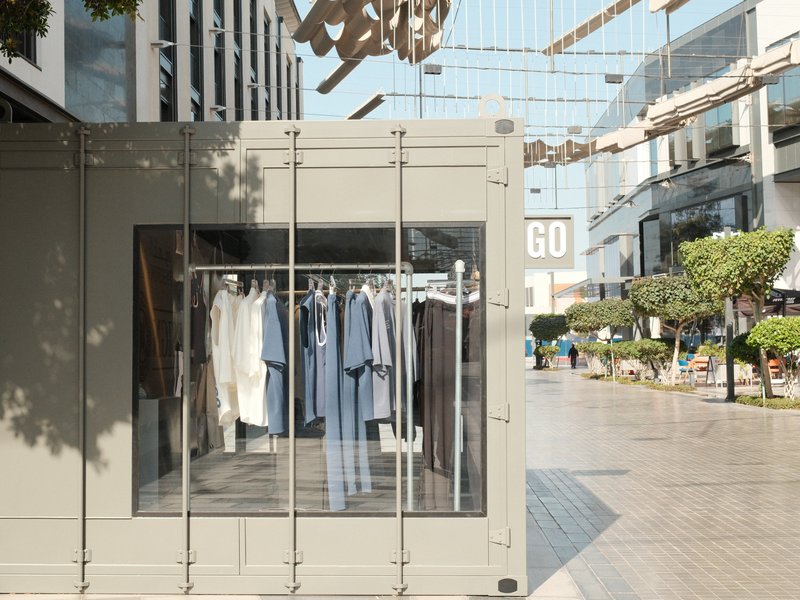 A modern clothing store display in a shipping container with hanging clothes, set in a bustling urban area.