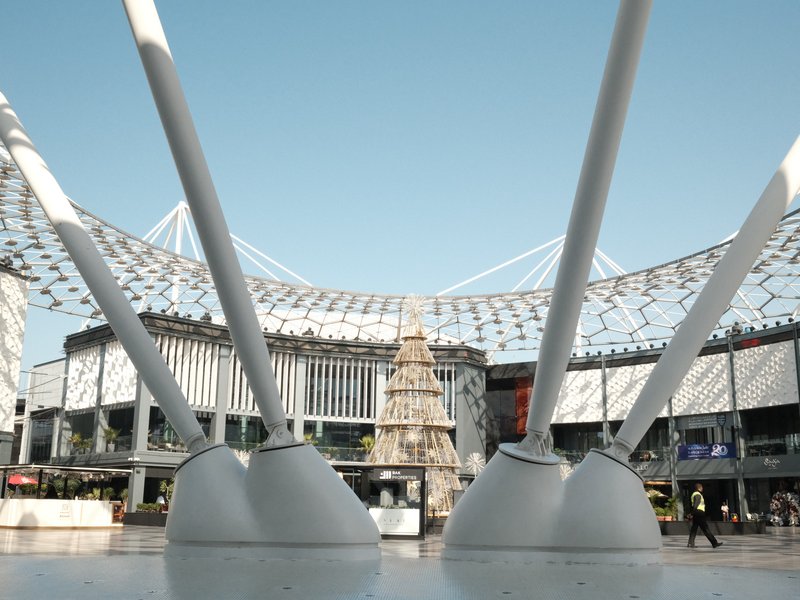 View of a modern urban plaza with large structural supports framing a Christmas tree in the center.