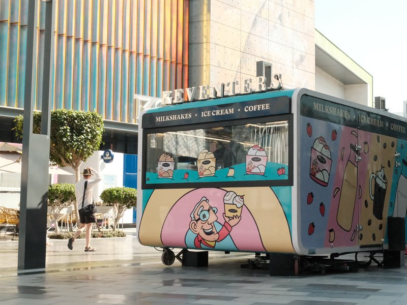 A colorful food truck with cartoonish designs parked in an urban area, with a person walking nearby.