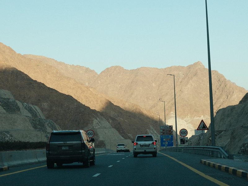 A highway scene with vehicles driving through a mountainous area under clear skies.