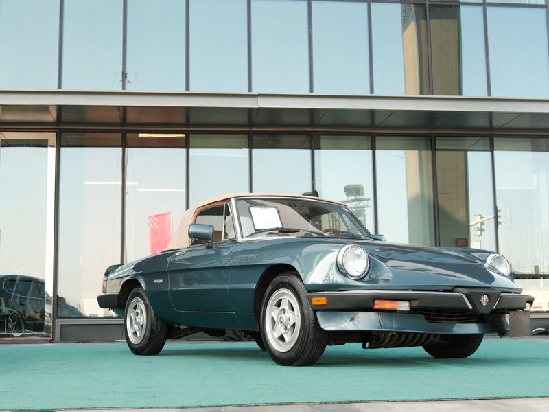A vintage blue car parked in front of a modern glass building, showcasing its classic design.