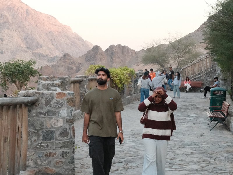 Two people walking on a stone path with mountains in the background during sunset.