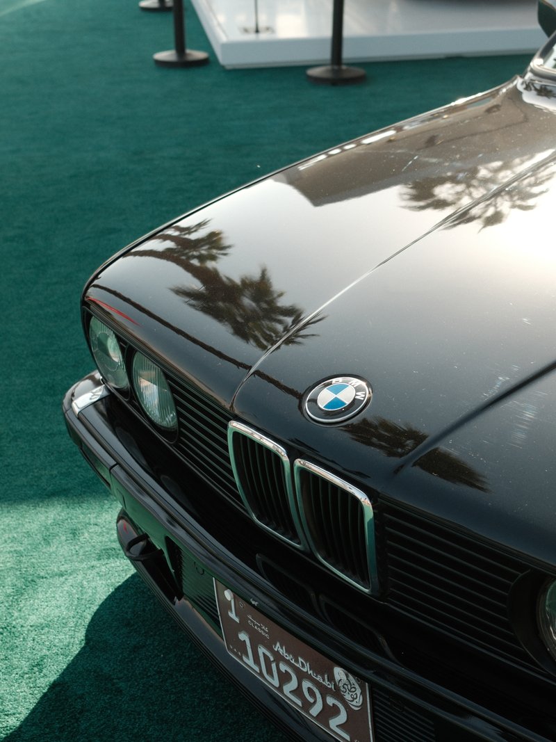 Close-up of a black BMW car hood with shiny details on a green carpet background.