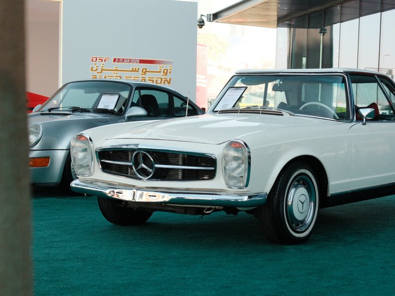 A classic white Mercedes-Benz car parked indoors with a silver car in the background.