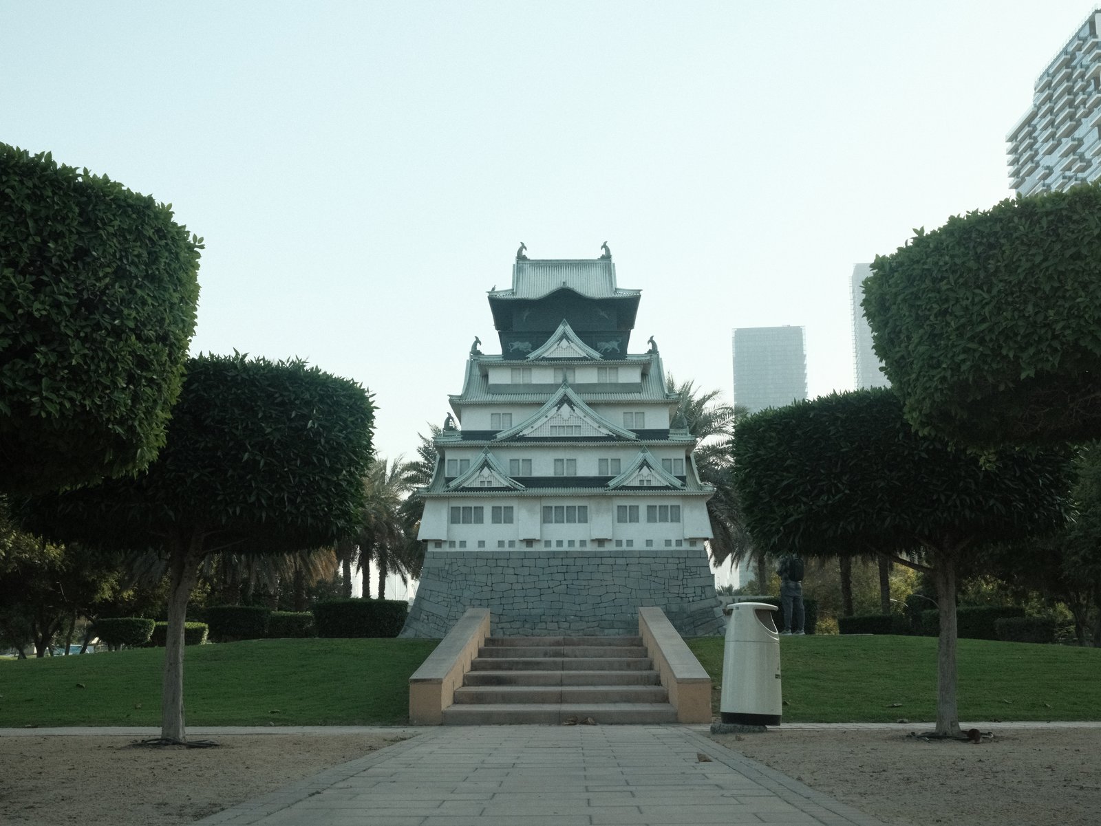 A traditional-style building with a tiered roof, surrounded by neatly trimmed bushes and palm trees.