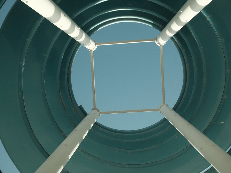 Looking up from inside a cylindrical structure with white supports against a clear blue sky.