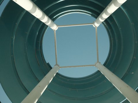 Looking up from inside a cylindrical structure with white supports against a clear blue sky.