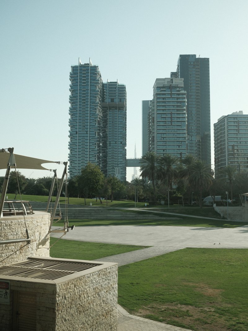 View of modern skyscrapers with a green park in the foreground under clear skies.