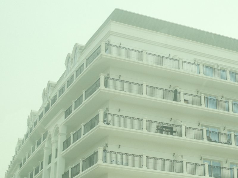 A close-up view of a modern white building with balconies, shrouded in a hazy atmosphere.