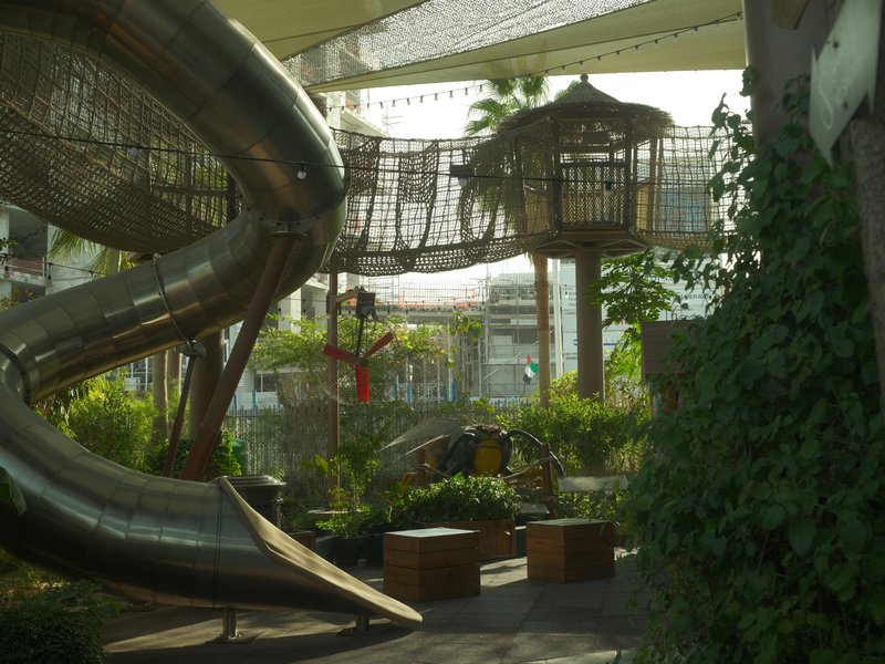 A playground area featuring a large metal slide and a treehouse surrounded by greenery.