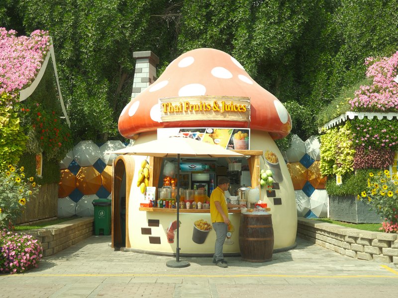 A whimsical mushroom-shaped food stall surrounded by colorful flowers and greenery.