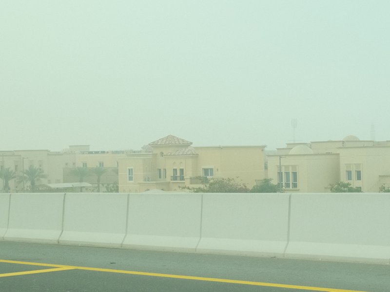 A hazy view of buildings behind a white barrier on a road, with a muted atmosphere.