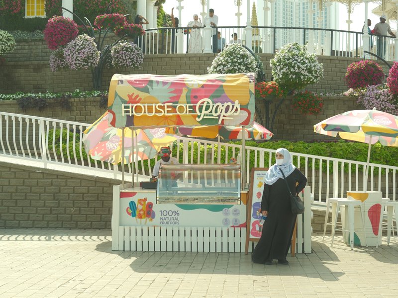 A colorful outdoor pop stand with a vendor and a customer in a sunny setting.