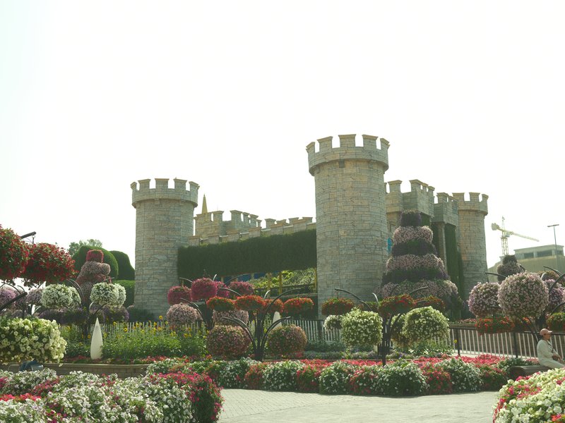 A stone castle surrounded by colorful flower beds in a garden setting.
